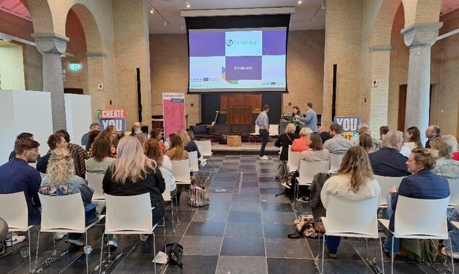 Eindevent Care2adapt, groep mensen zit samen en kijkt naar presentatie.