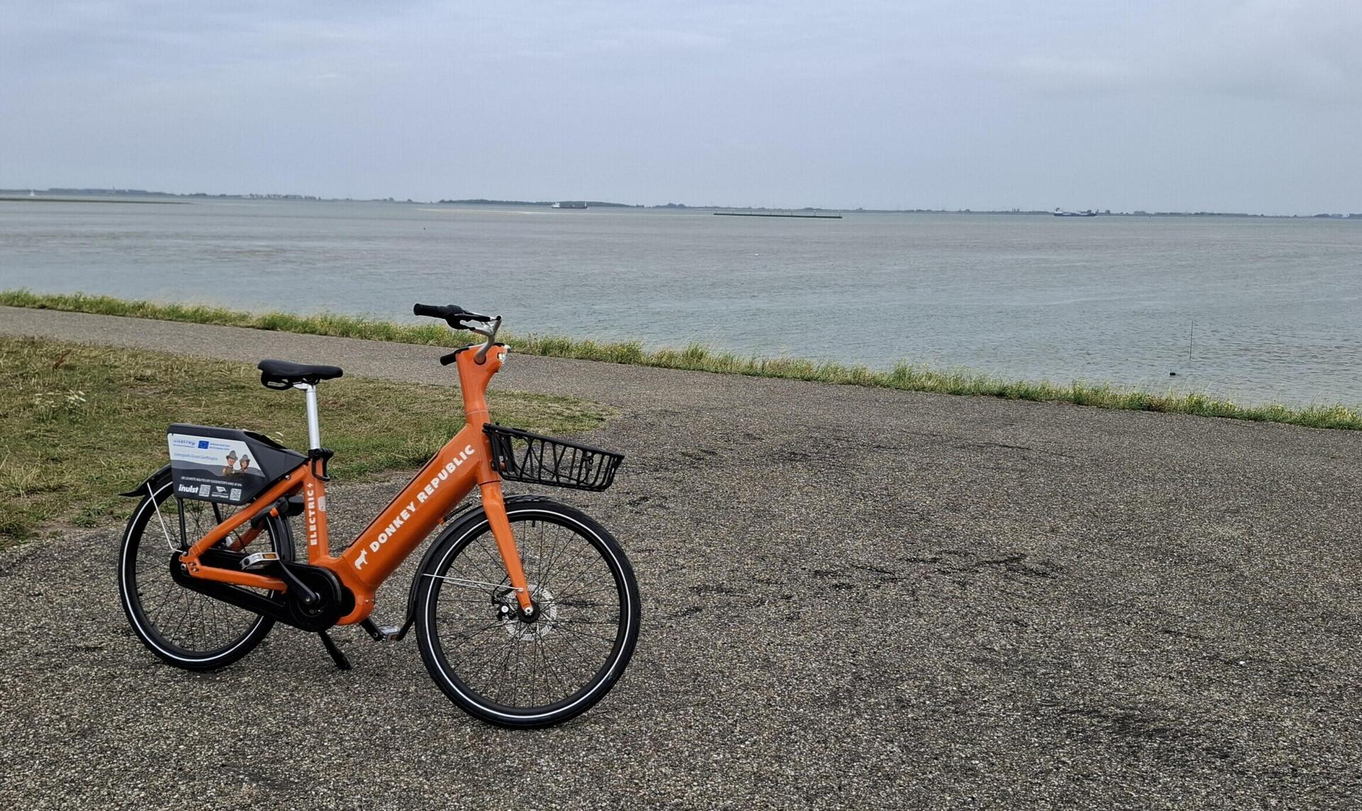 Een oranje deelfiets van Donkey Republic bij de Westerschelde