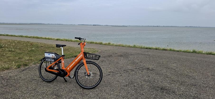 Een oranje deelfiets van Donkey Republic bij de Westerschelde