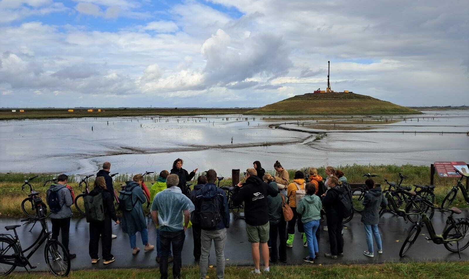 Een groep mensen kijkt tijdens een excursie uit over de Panoramaheuvel, gelegen in een slikkengebied.