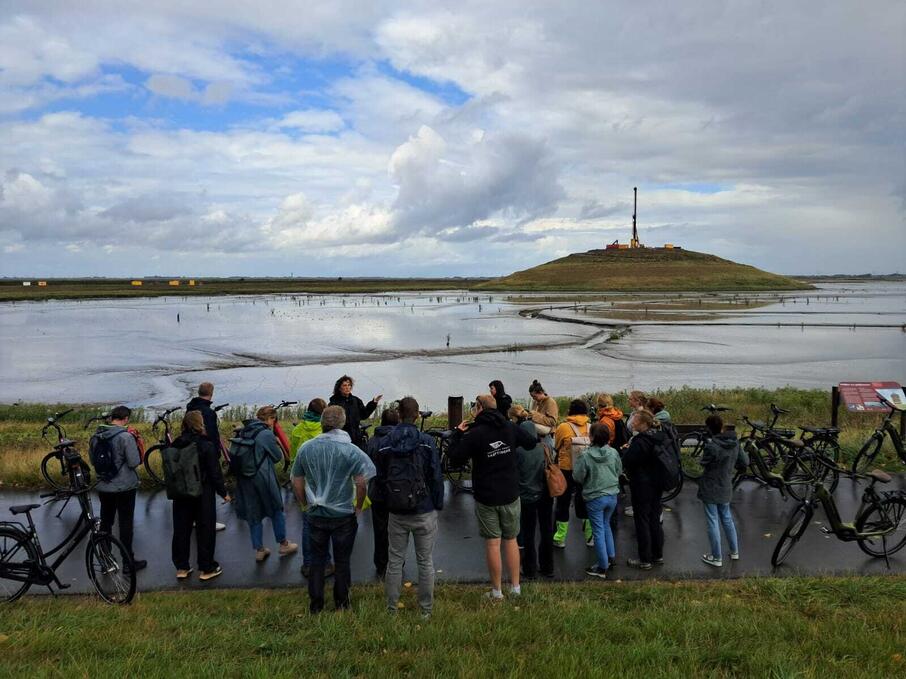 Een groep mensen kijkt tijdens een excursie uit over de Panoramaheuvel, gelegen in een slikkengebied.
